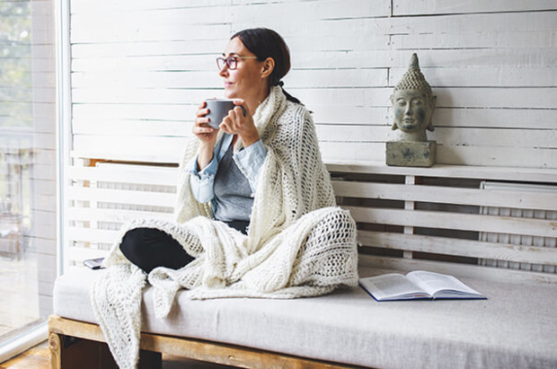 Frau sitzt mit Tee und Decke in Wintergarten